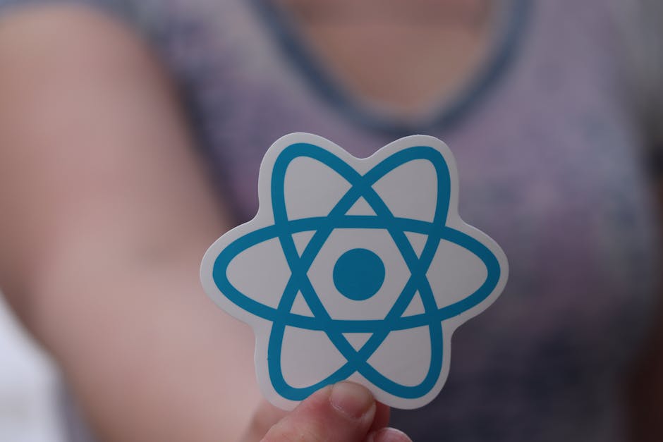 UX design principles - A person holds a sticker featuring the React logo, commonly used in web development.