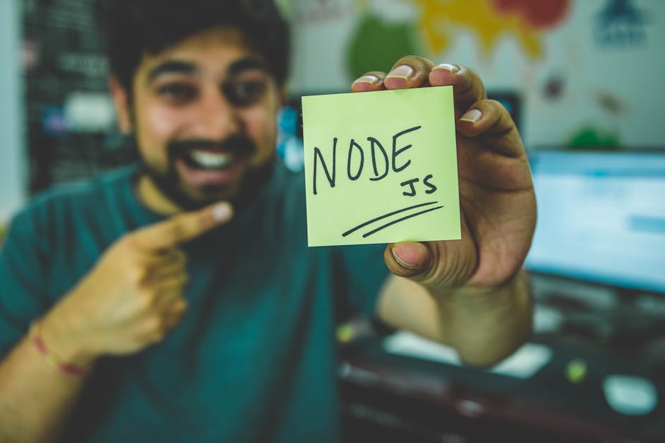 MVP development for startups - A cheerful software developer shows a Node.js sticky note in a tech workspace.